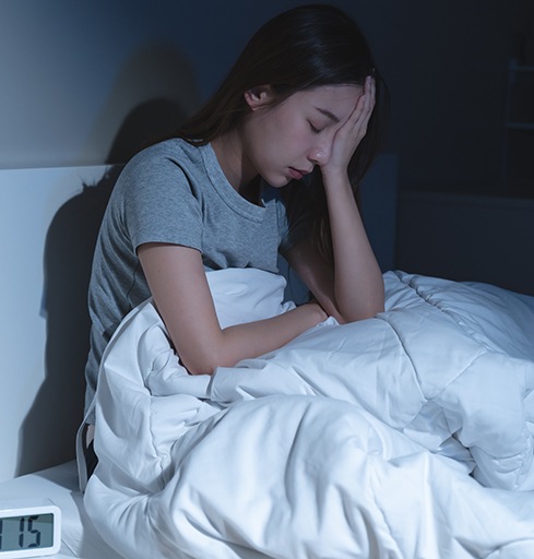 Woman sitting up in bed, struggling to sleep