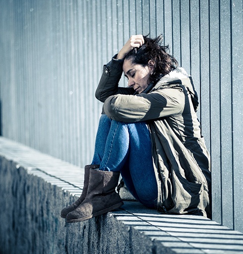 Sad woman sitting outdoors, holding her head