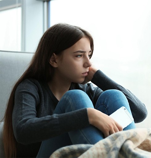 depressed teen girl sitting next to window v1